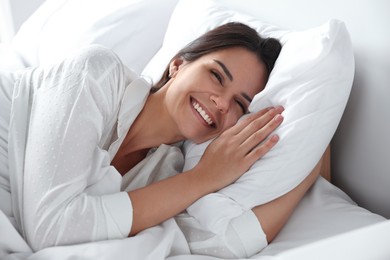 Happy young woman lying on soft pillow in bed at home