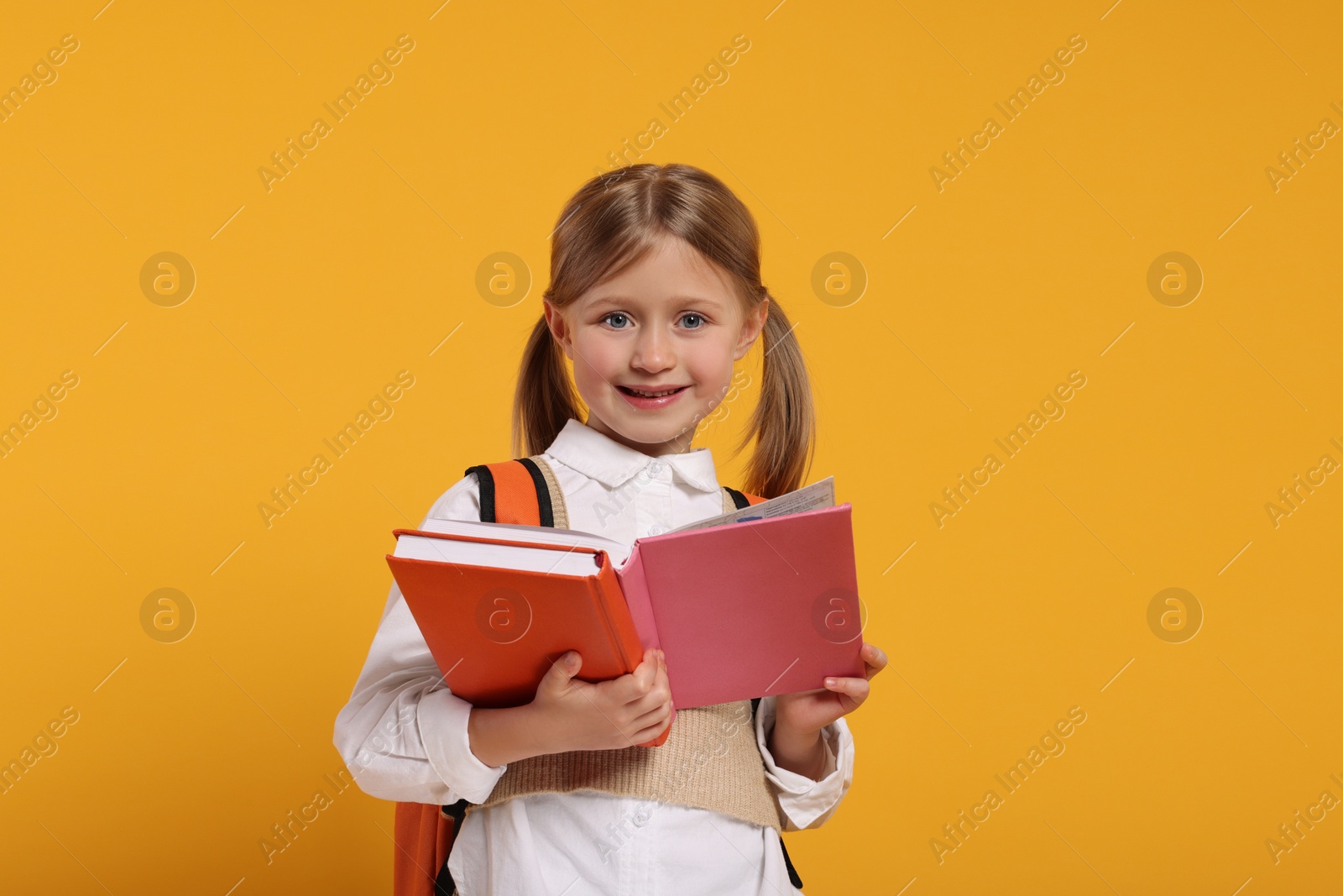 Photo of Happy schoolgirl with backpack and books on orange background