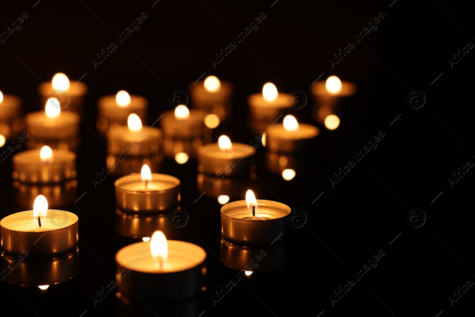 Photo of Burning candles on mirror surface in darkness, closeup. Space for text