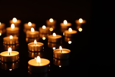 Photo of Burning candles on mirror surface in darkness, closeup. Space for text