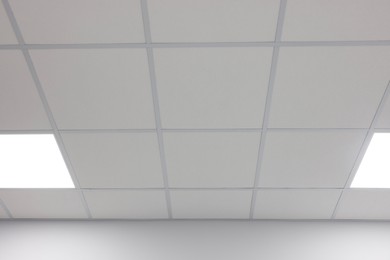 Photo of White ceiling with PVC tiles and lighting indoors, low angle view