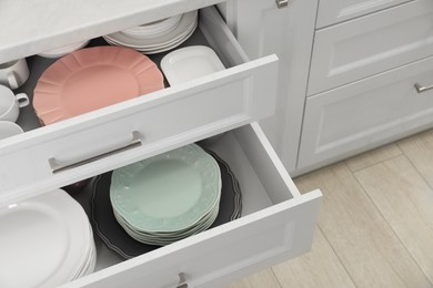 Photo of Stacks of clean plates in drawers indoors