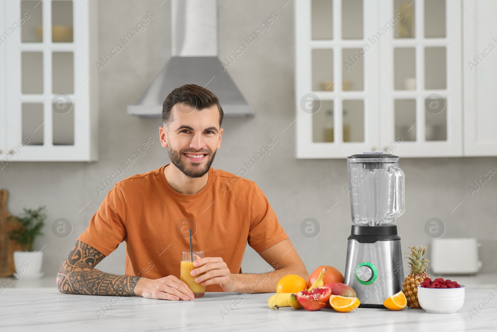 Photo of Handsome man with delicious smoothie at white marble table in kitchen