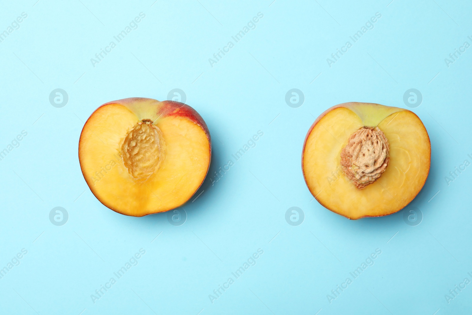 Photo of Halves of sweet juicy peach on light blue background, top view