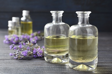 Photo of Bottles with natural lavender oil and flowers on grey wooden table against dark background, closeup view. Space for text