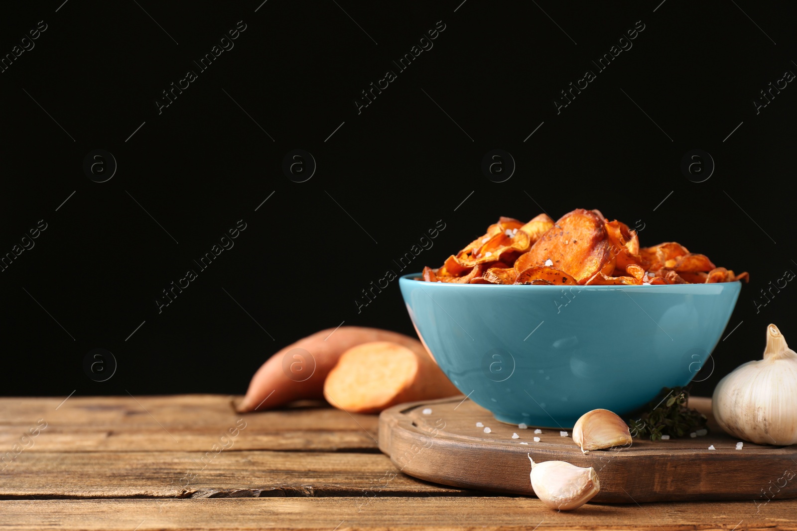 Photo of Composition with sweet potato chips and garlic on table against black background. Space for text