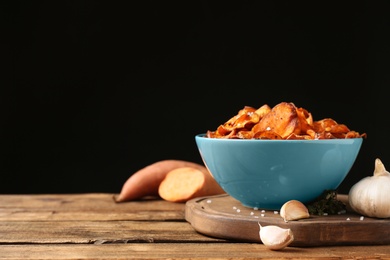 Composition with sweet potato chips and garlic on table against black background. Space for text