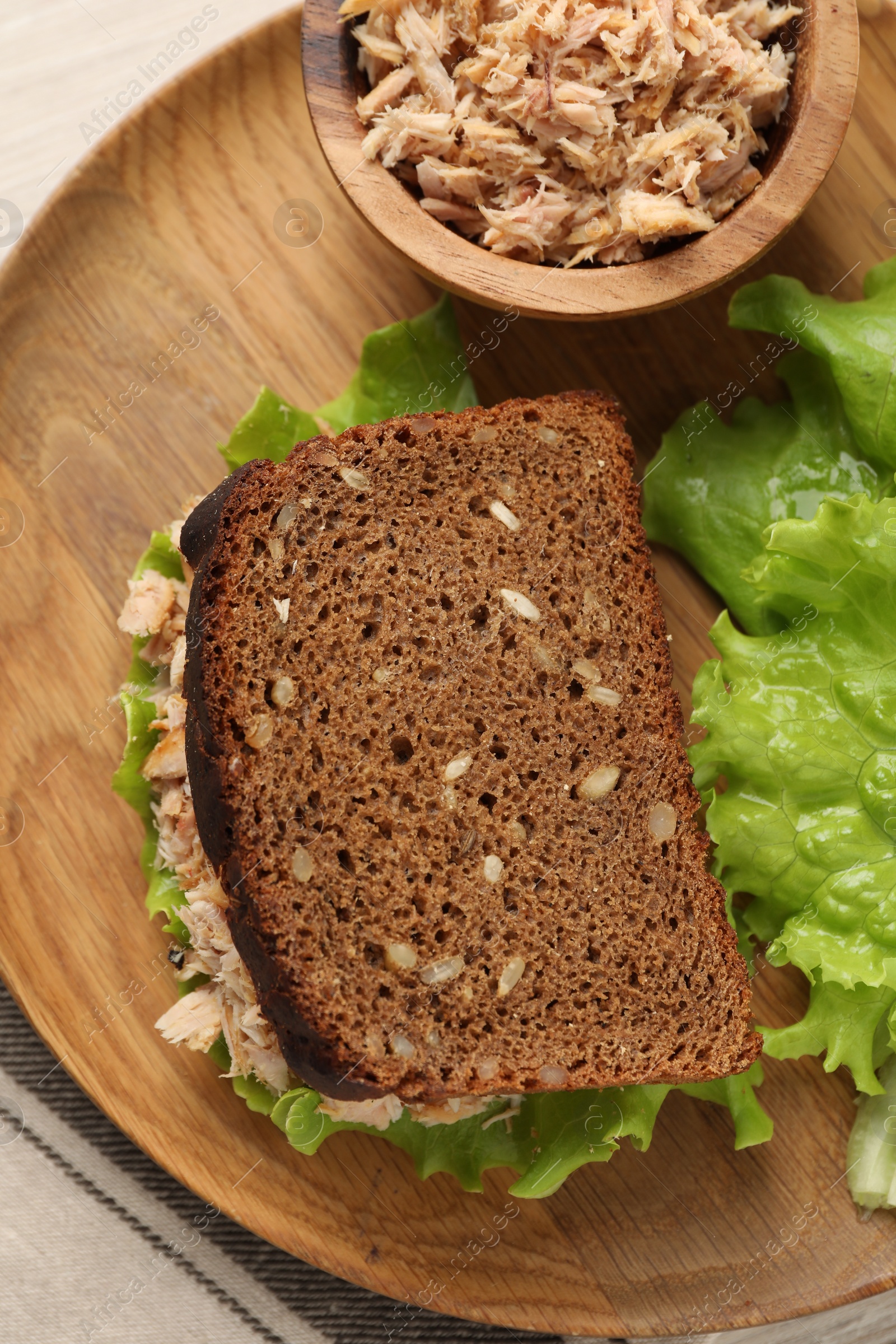 Photo of Delicious sandwich with tuna and lettuce leaves on wooden plate, top view