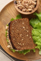 Delicious sandwich with tuna and lettuce leaves on wooden plate, top view