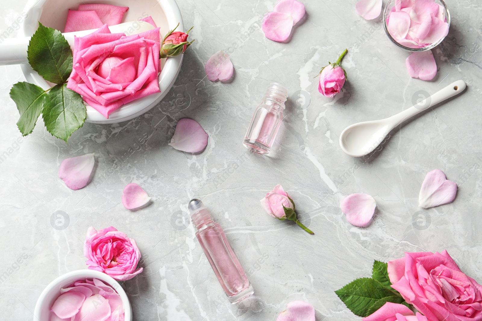 Photo of Flat lay composition with rose essential oil and fresh flowers on grey table