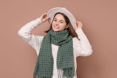 Beautiful woman in warm scarf and hat on brown background