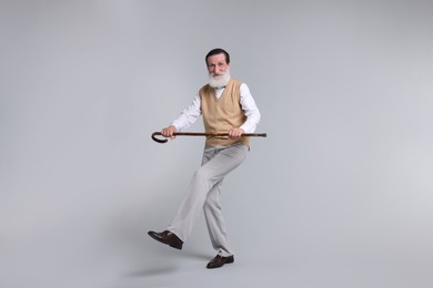Photo of Cheerful senior man with walking cane on light gray background
