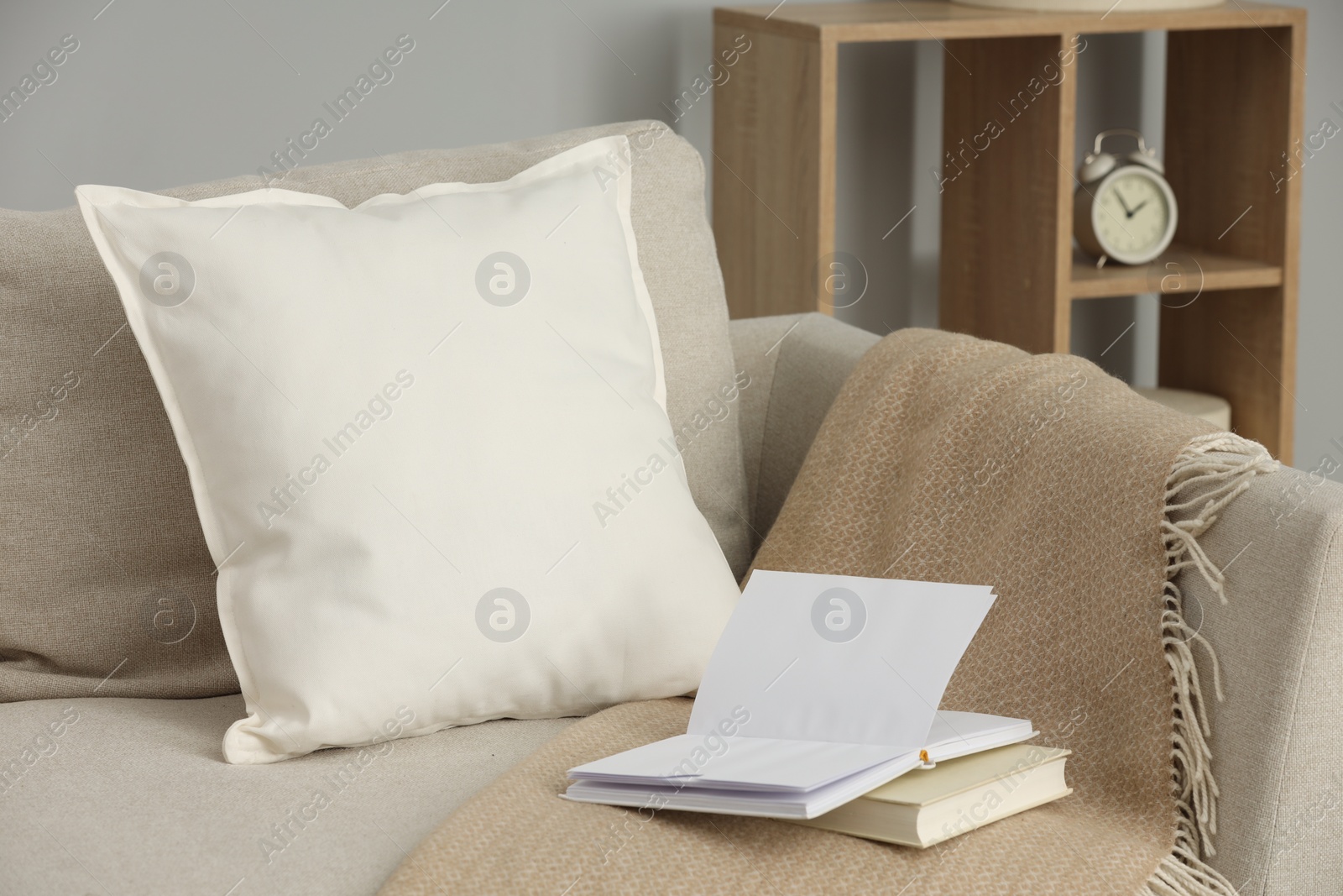 Photo of Soft white pillow, blanket and books on sofa indoors