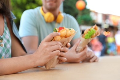 Young couple holding delicious bubble waffles with tomato and arugula at table outdoors, closeup