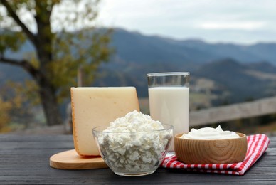 Photo of Tasty cottage cheese and other fresh dairy products on black wooden table in mountains