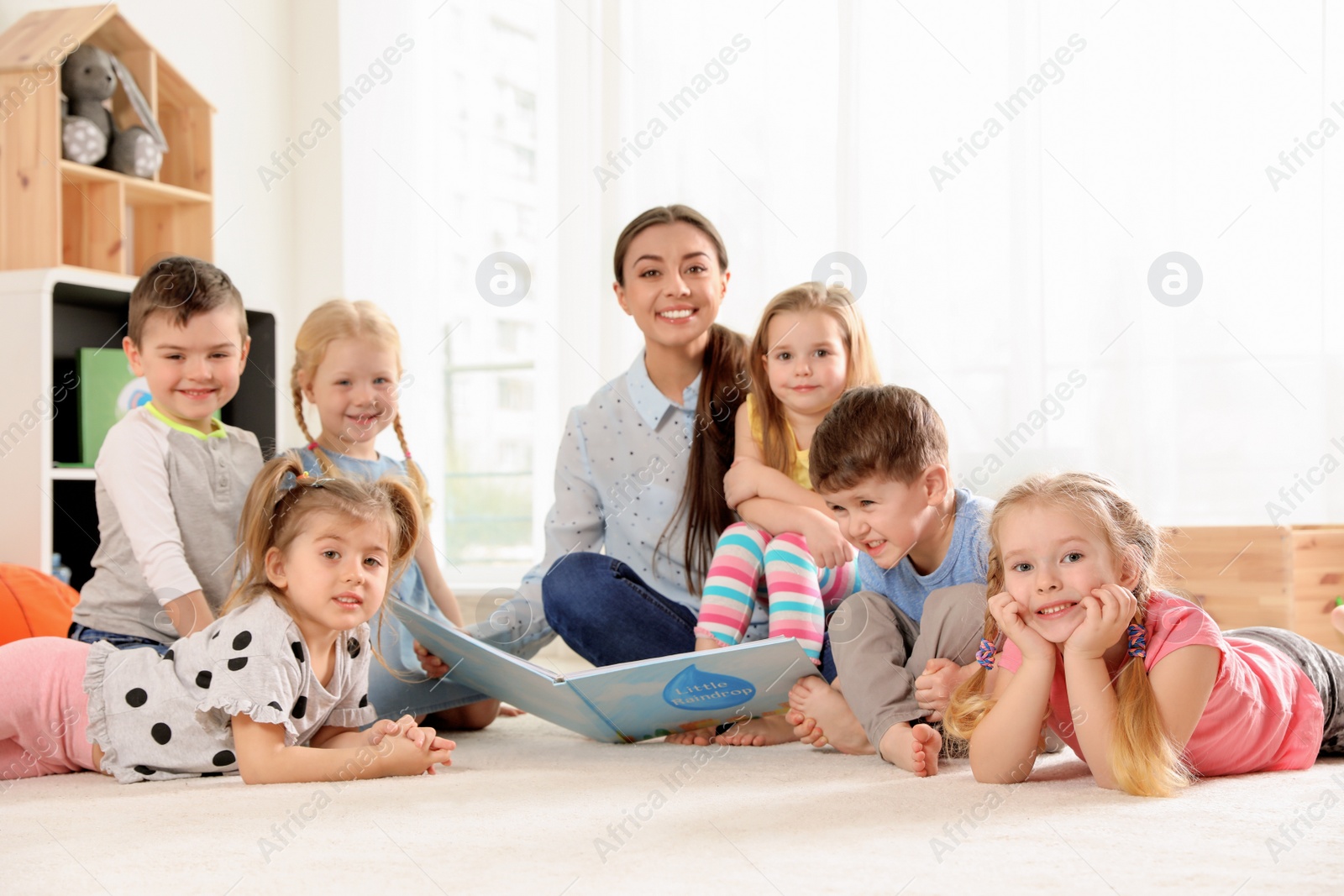 Photo of Kindergarten teacher reading book to children indoors. Learning and playing