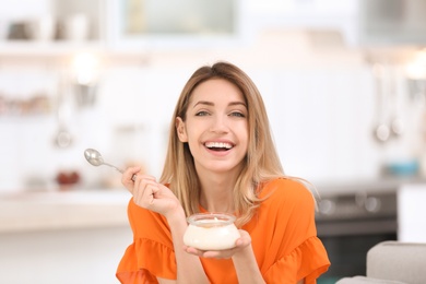 Photo of Young attractive woman eating tasty yogurt in kitchen