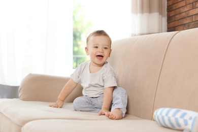 Photo of Adorable little baby sitting on sofa at home