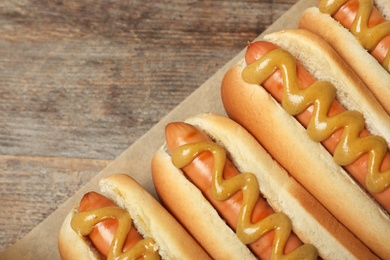 Photo of Hot dogs with mustard and space for text on wooden background, top view