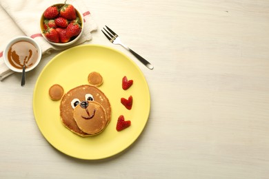 Creative serving for kids. Plate with strawberries, cute bear made of pancakes on light wooden table, flat lay. Space for text