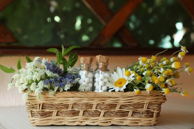 Photo of Bottles with homeopathic remedy and flowers in basket on wooden table
