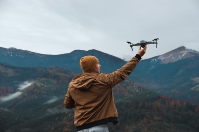 Photo of Young man with modern drone in mountains, back view