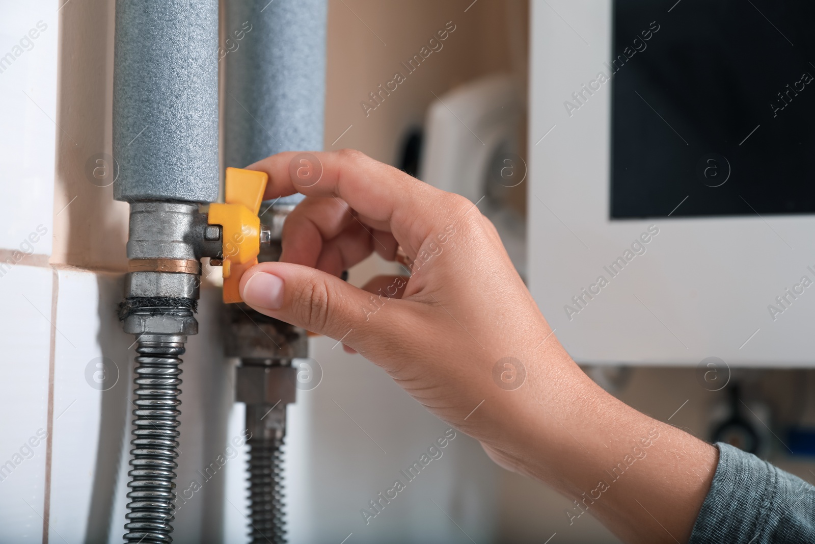 Photo of Woman turning on valve of gas boiler indoors, closeup