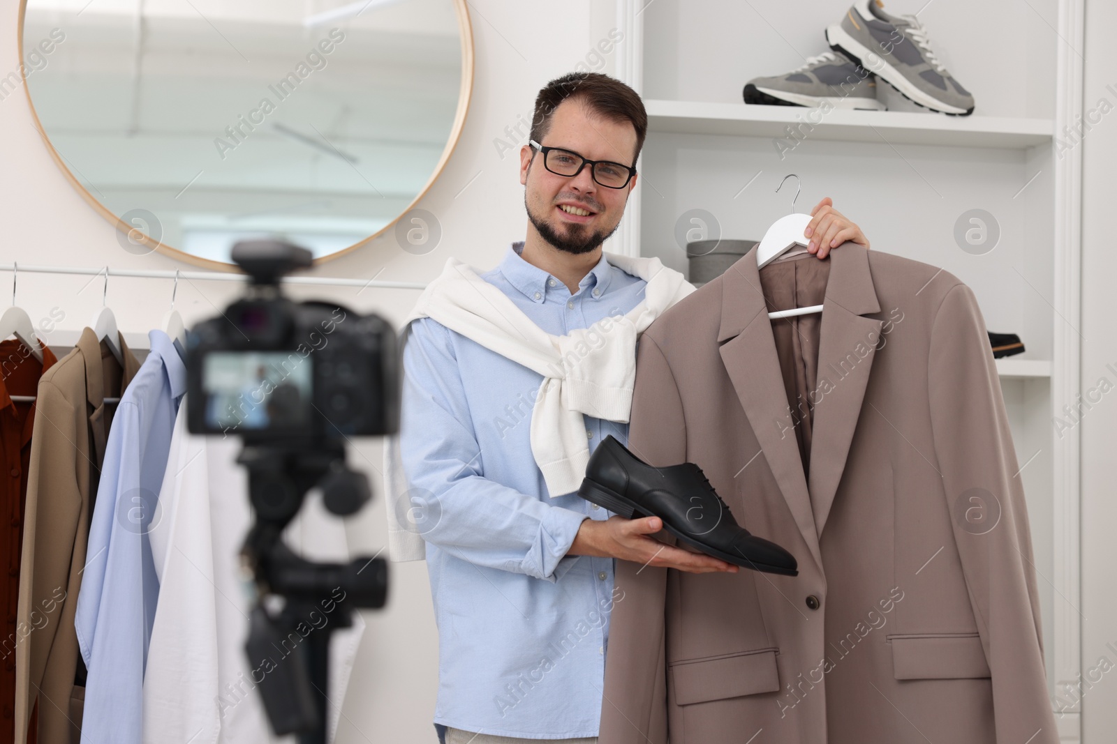 Photo of Smiling fashion blogger showing clothes while recording video at home