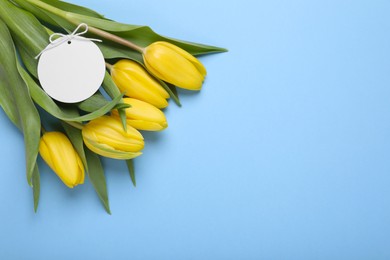 Photo of Bouquet of beautiful yellow tulips and blank card on light blue background, top view with space for text. Birthday celebration