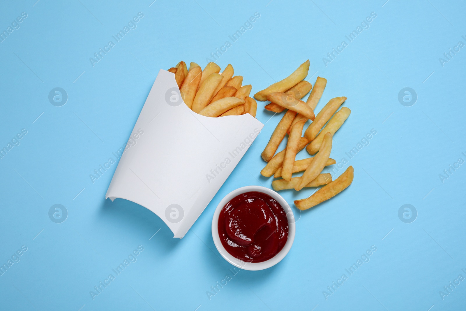 Photo of Paper cup with French fries and ketchup on light blue table, flat lay. Space for text