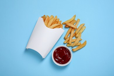 Paper cup with French fries and ketchup on light blue table, flat lay. Space for text