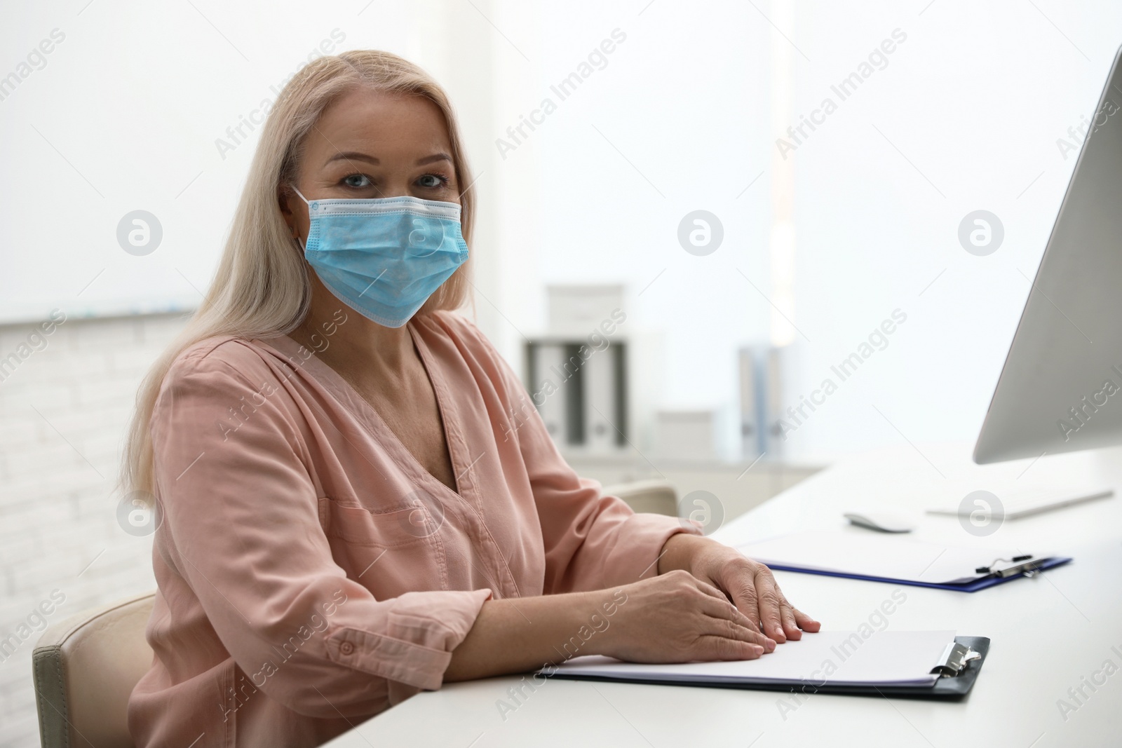 Photo of Mature woman wearing medical mask at workplace. Dangerous virus