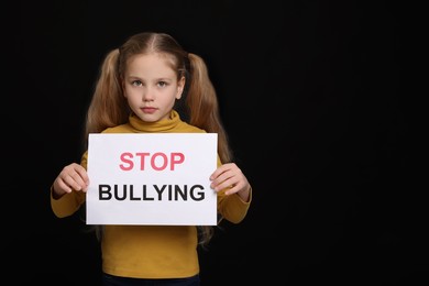 Girl holding sign with phrase Stop Bullying on black background, space for text