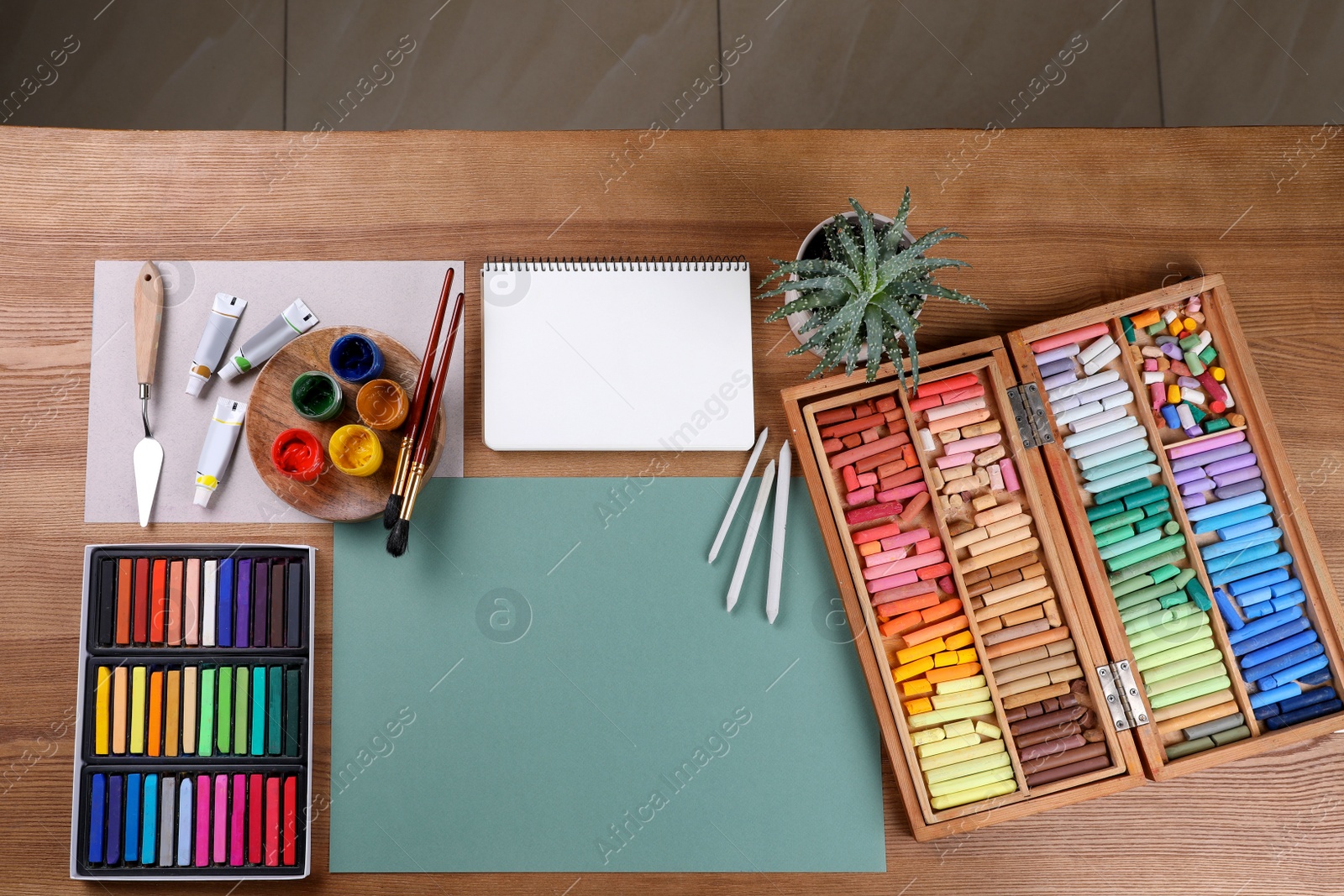 Photo of Blank sheet of paper, colorful chalk pastels and other drawing tools on wooden table, flat lay. Modern artist's workplace