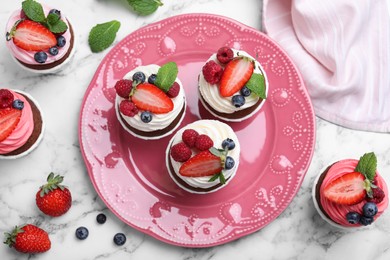 Photo of Delicious cupcakes with cream and berries on white marble table, flat lay