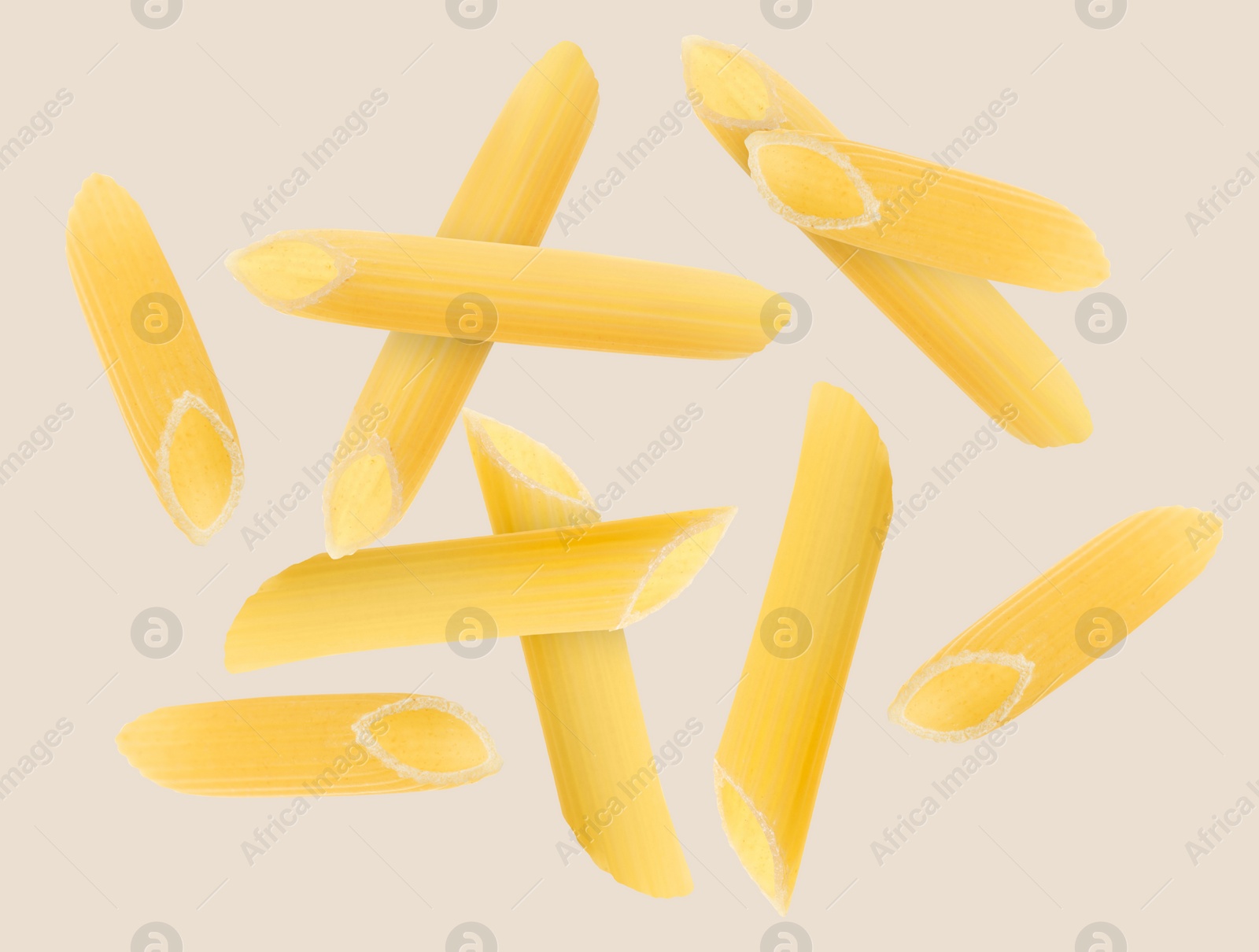 Image of Raw penne pasta flying on beige background