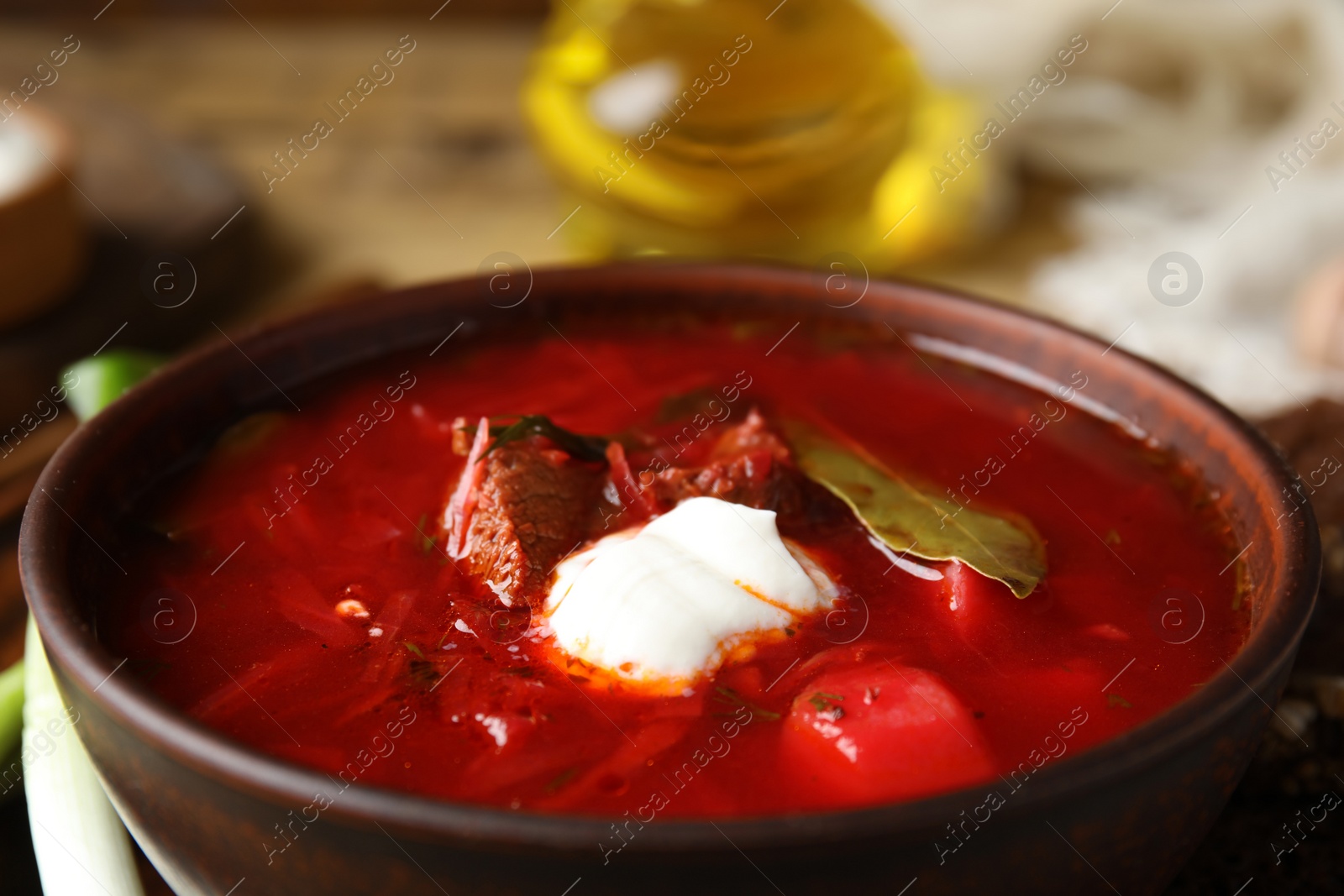 Photo of Clay bowl with Ukrainian borsch on table, closeup