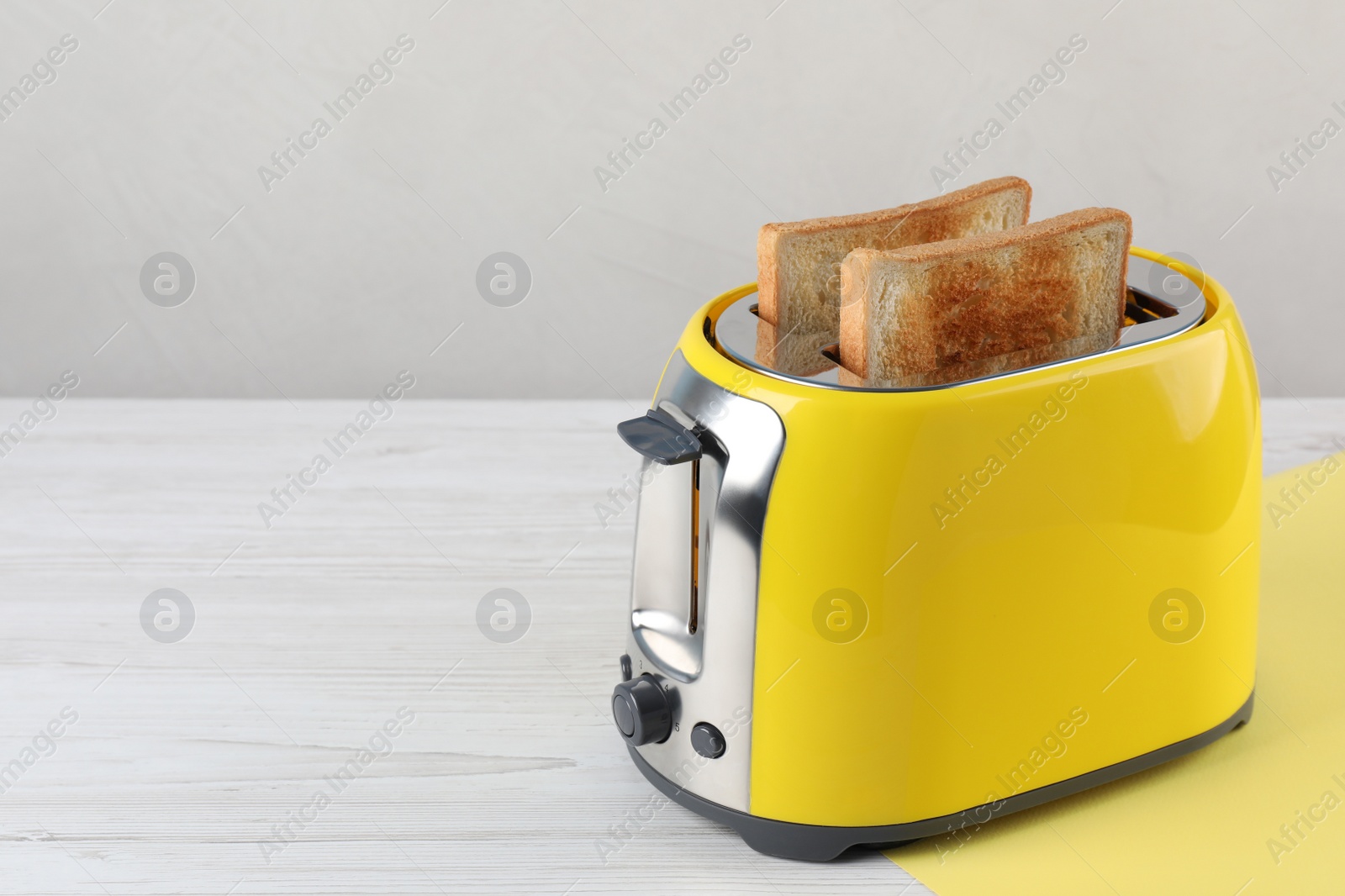 Photo of Modern toaster with slices of bread on white wooden table. Space for text