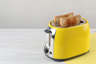 Modern toaster with slices of bread on white wooden table. Space for text