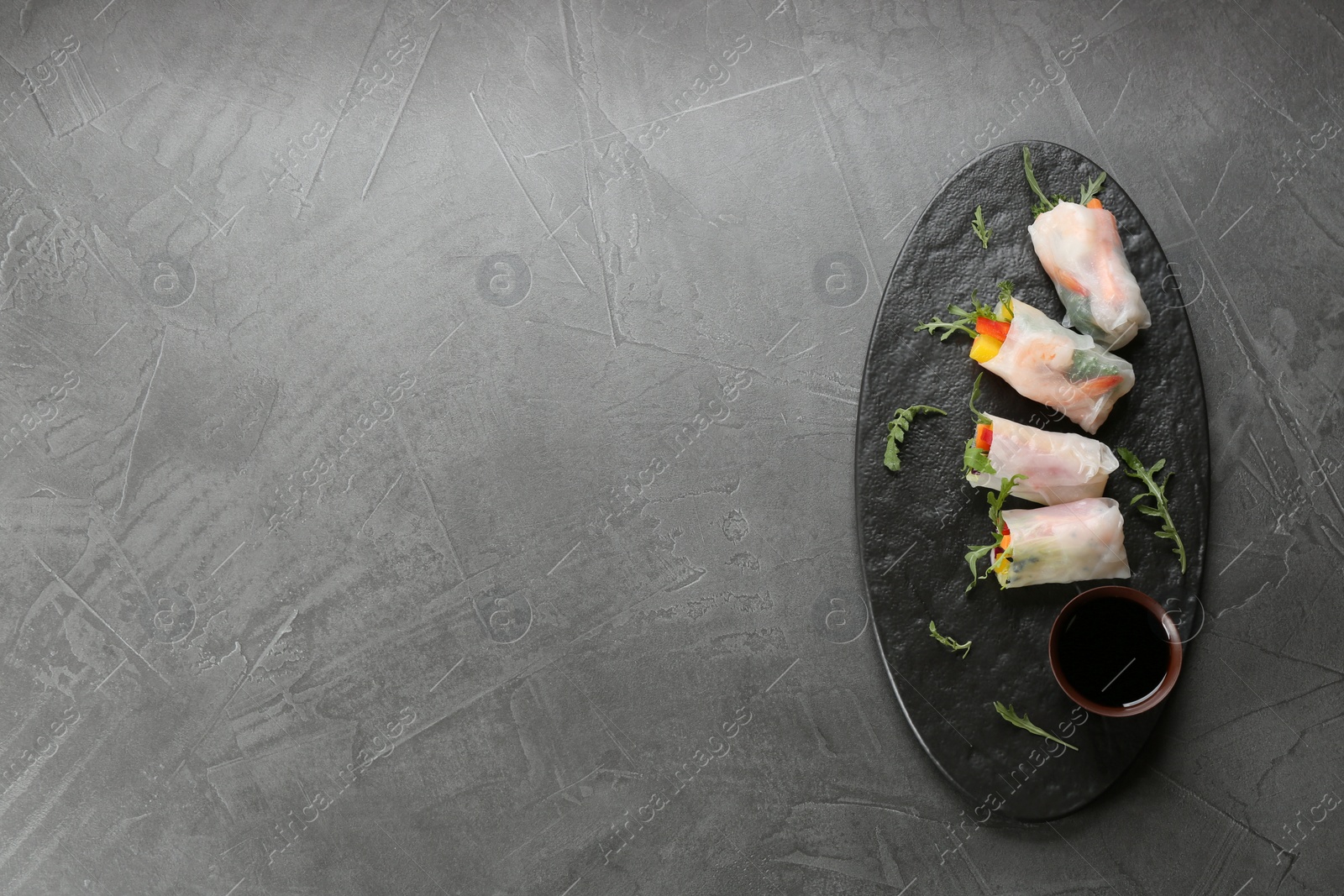 Photo of Delicious rolls wrapped in rice paper served on grey table, top view. Space for text