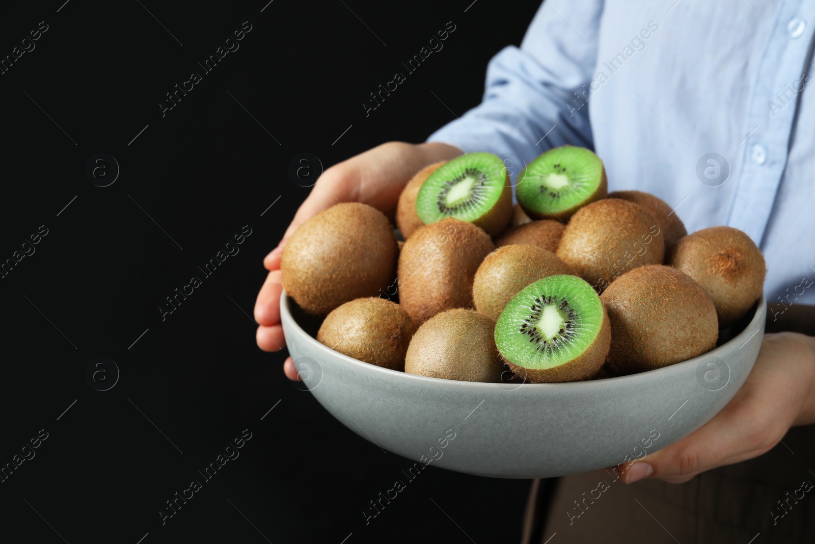 Photo of Woman holding bowl with fresh ripe kiwis on black background, closeup. Space for text
