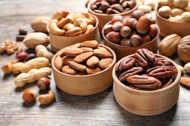 Photo of Bowls with organic nuts on wooden table. Snack mix