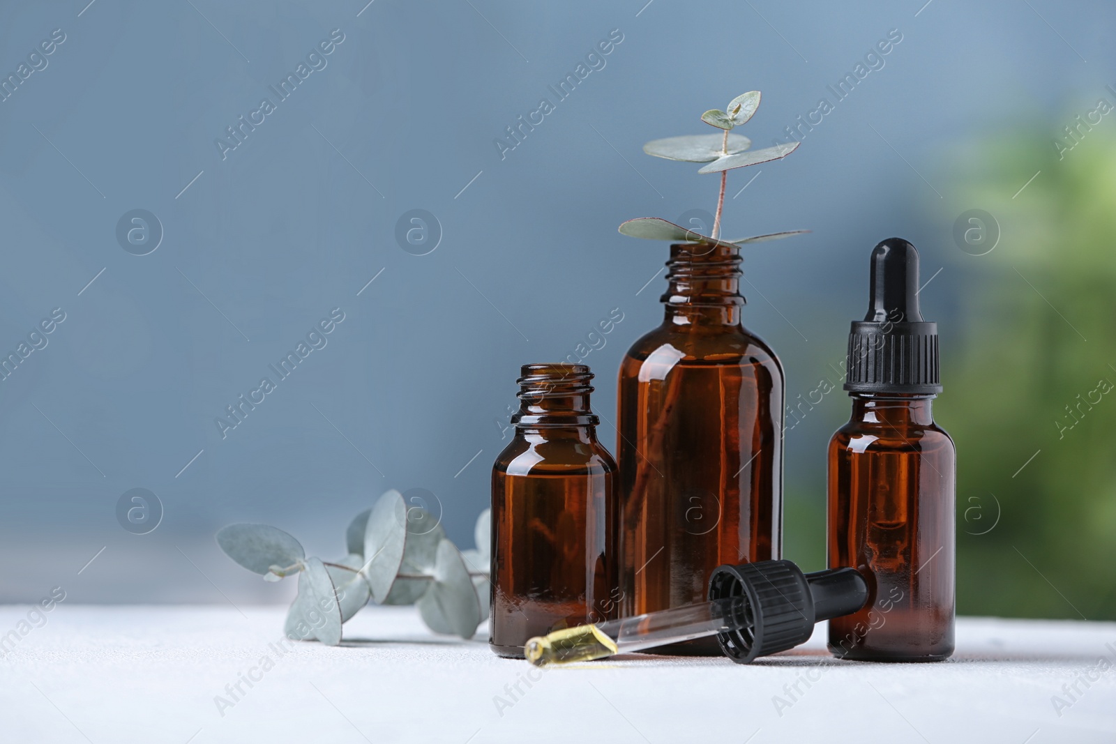 Photo of Bottles of essential oil and eucalyptus on white table. Space for text