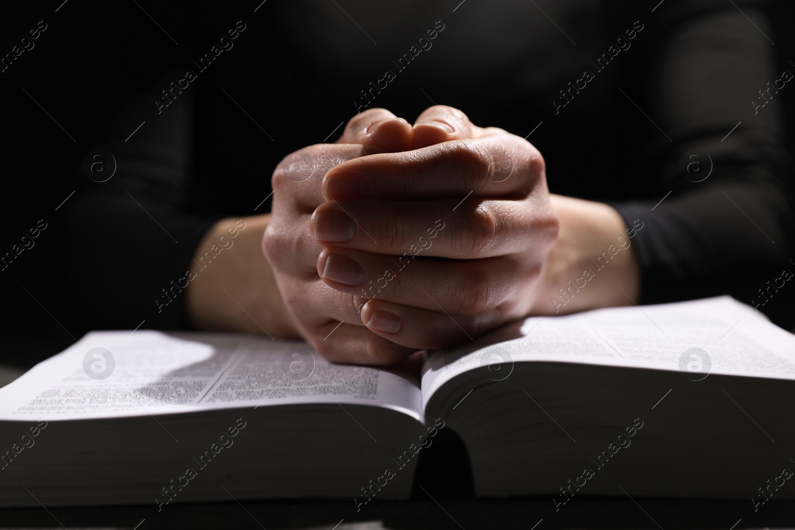 Photo of Religion. Christian woman praying over Bible at table, closeup