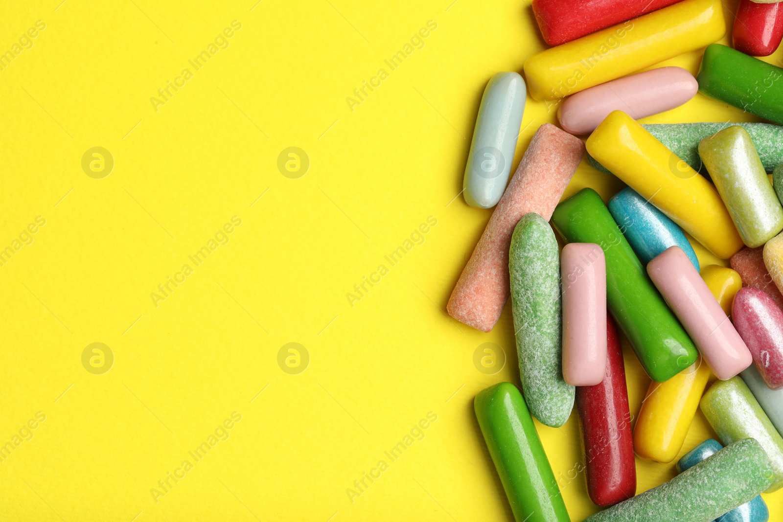 Photo of Many tasty bubble gums on yellow background, flat lay. Space for text