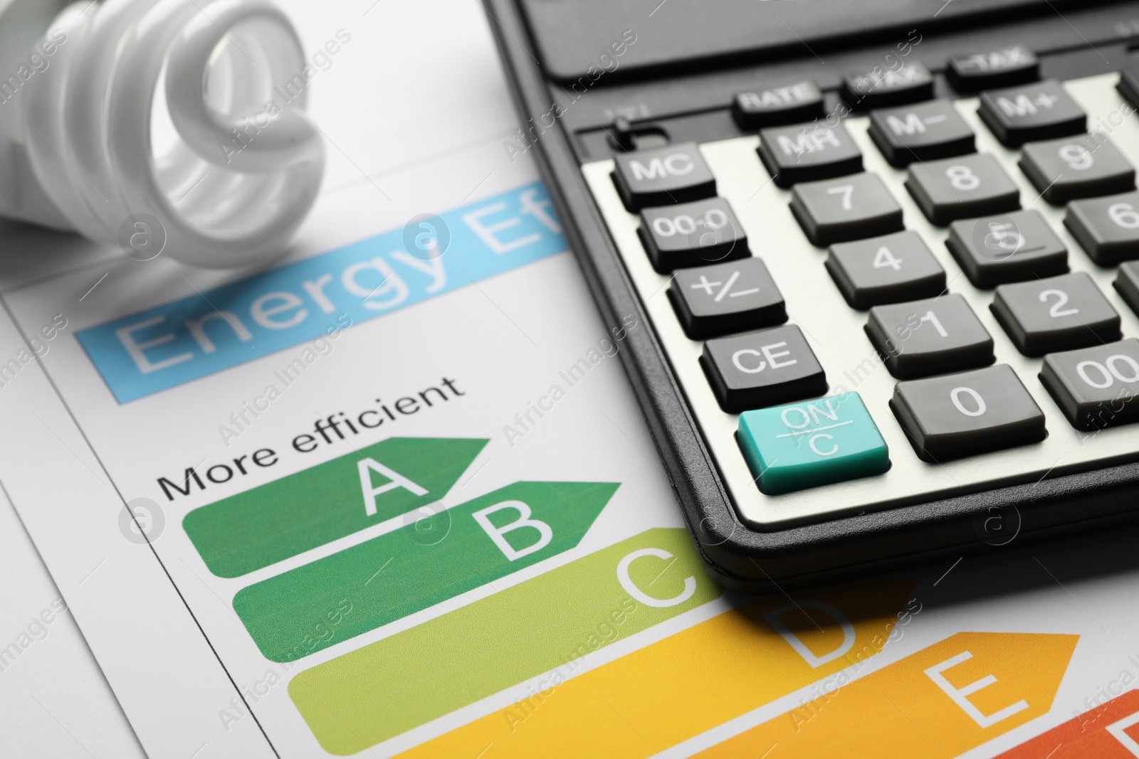 Photo of Energy efficiency rating chart, fluorescent light bulb and calculator, closeup