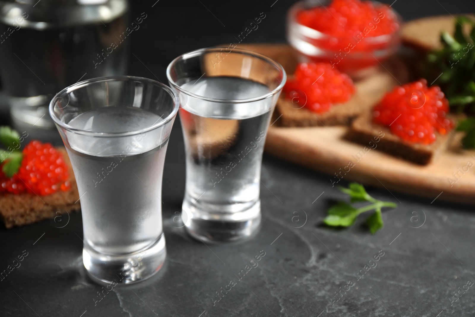 Photo of Cold Russian vodka and sandwiches with red caviar on black table, closeup