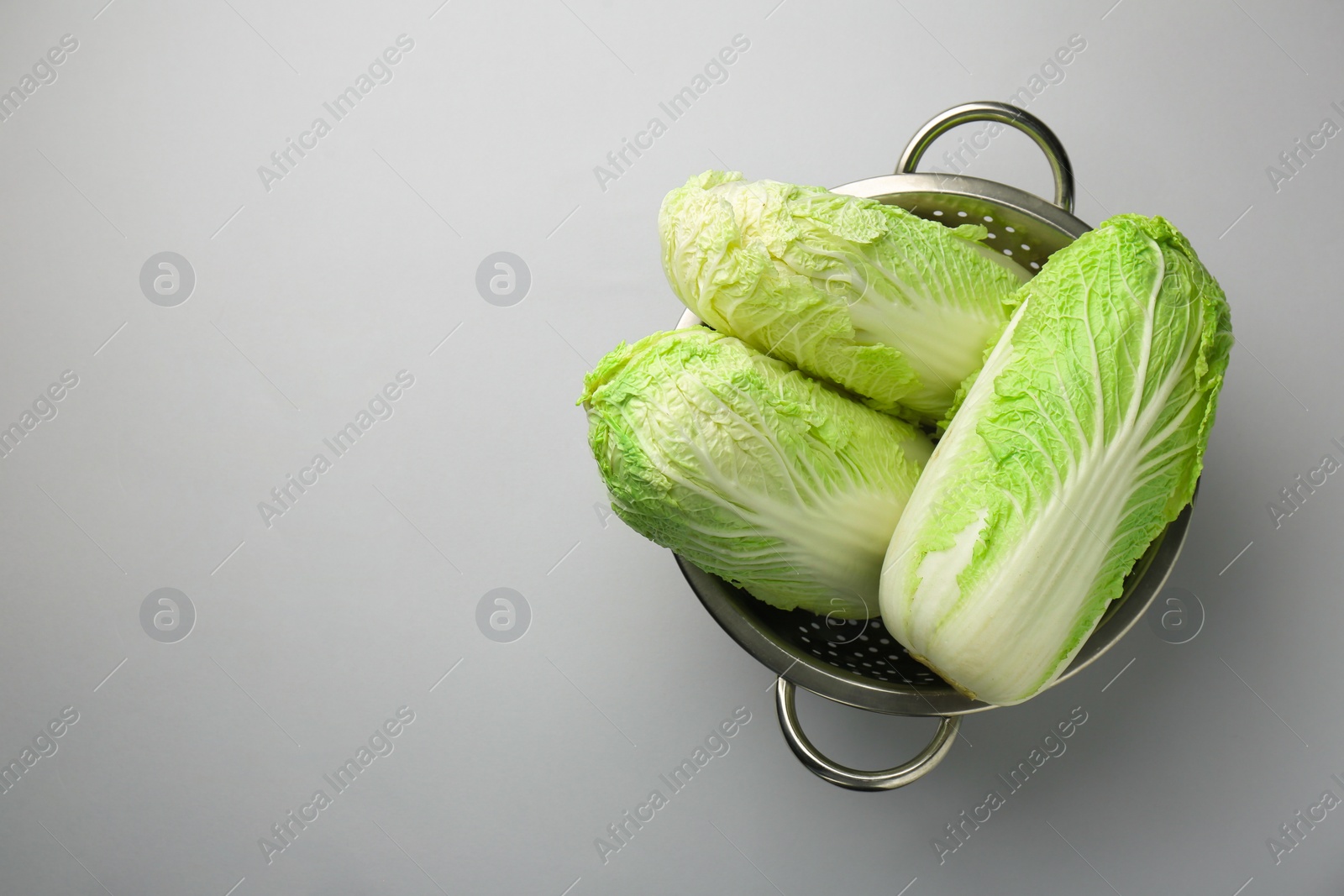 Photo of Fresh Chinese cabbages in colander on light background, top view. Space for text