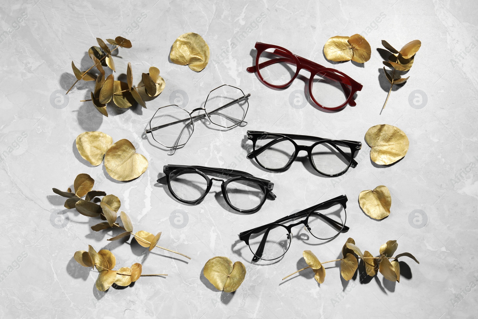 Photo of Many glasses in stylish frames and leaves on grey marble table, flat lay