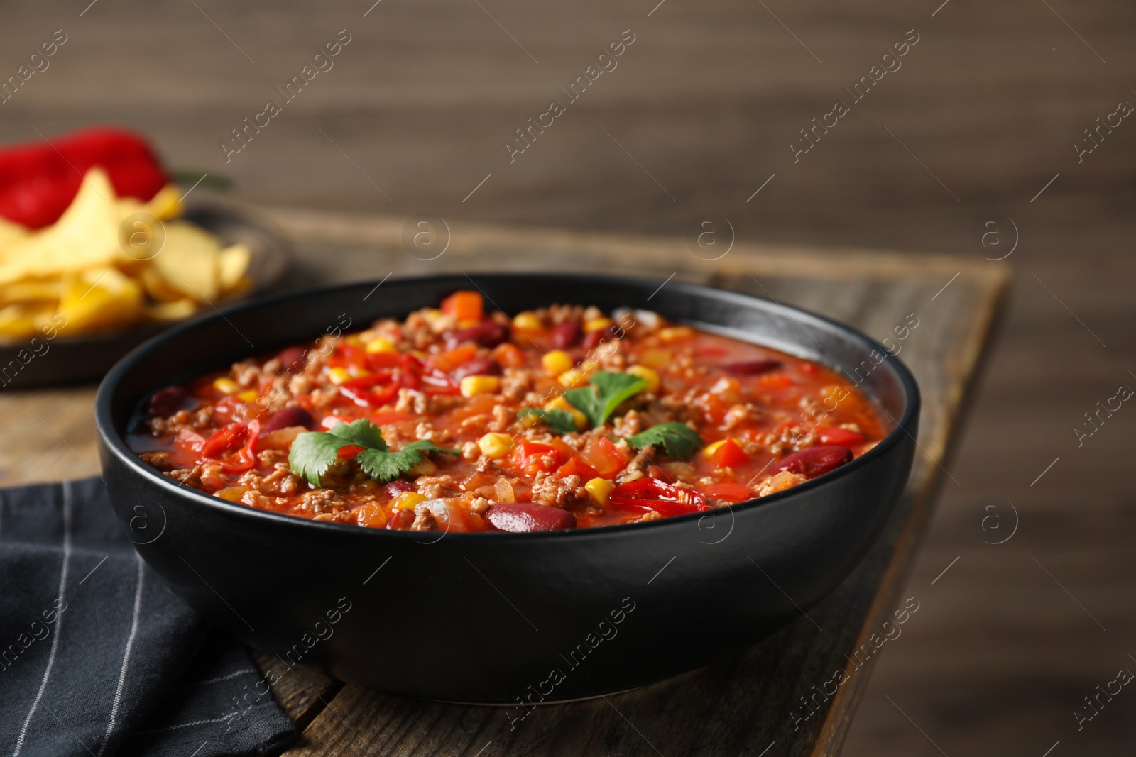 Photo of Bowl with tasty chili con carne on wooden table, closeup